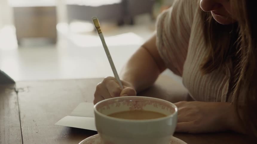 The woman is writing at her desk near a drink