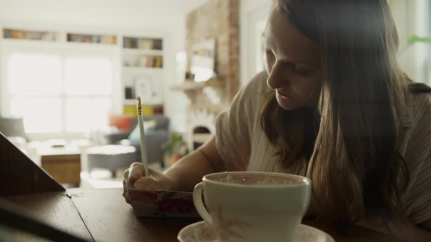 Woman sits at a desk writing on a sunny day