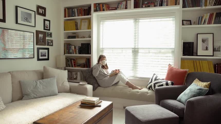 A woman sits on a window seat and drinks tea while reading