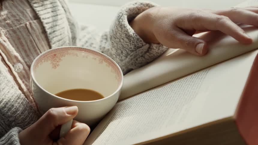 Woman holds a coffee mug and reads a book