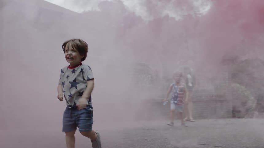 A young child runs through pink smoke
