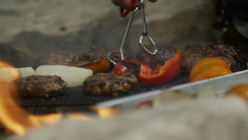 Person uses tongs to flip food over on a flaming grill