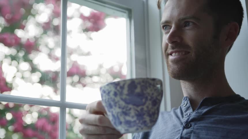 A man sips from a cup while looking out a window