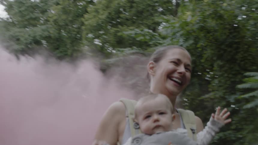 A woman runs through a pink dust cloud with a baby