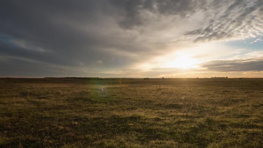 Clouds move across the sky over a field at sunset
