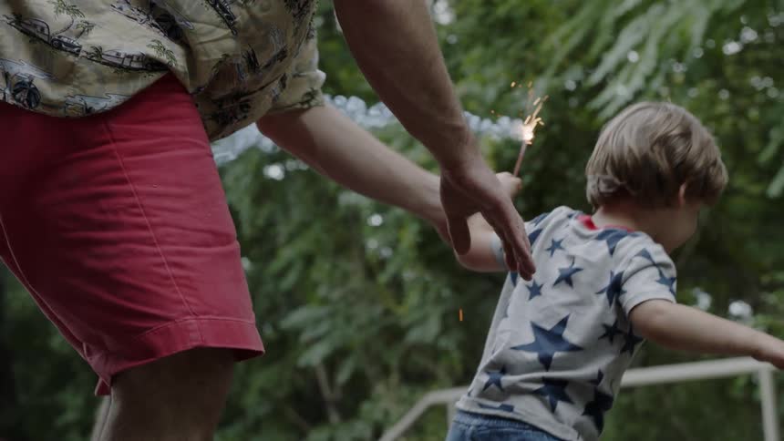 A man holds onto his son who is holding a sparkler