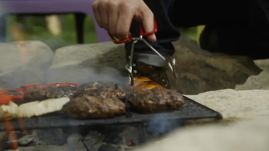 Man uses tongs to flip the peppers on the hot grill