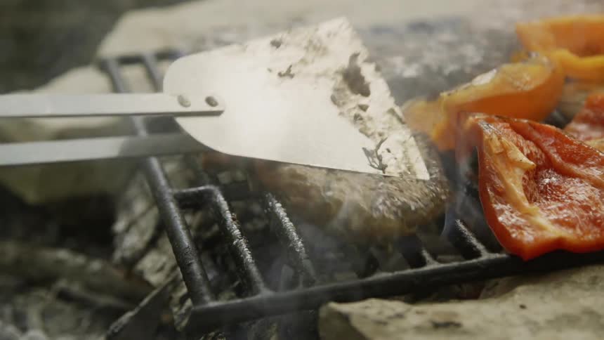 Large tongs are used to flip a burger on the grill
