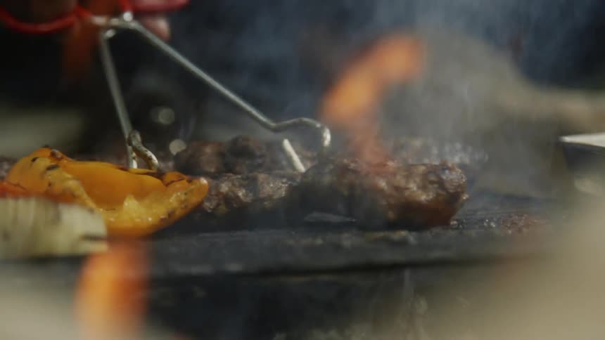 Person flips hamburgers over on a smoking grill