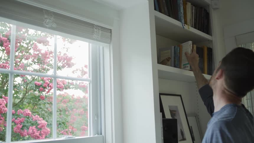 Man Takes Book Off a Bookshelf at Home