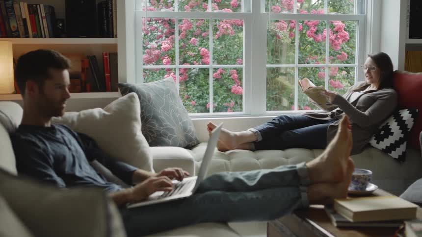 Man types on a laptop while sitting on a sofa