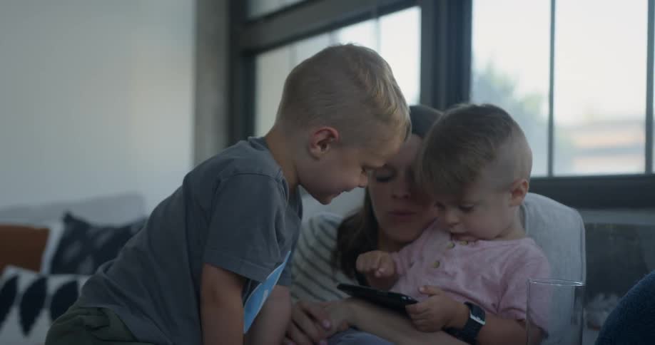 Woman holds two children on their lap as they play with a phone