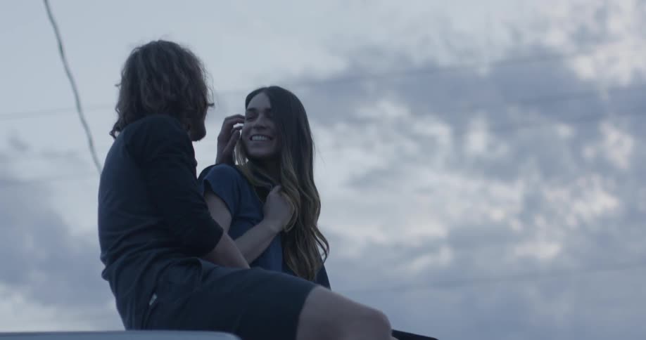 A man and woman flirt while sitting on a truck hood