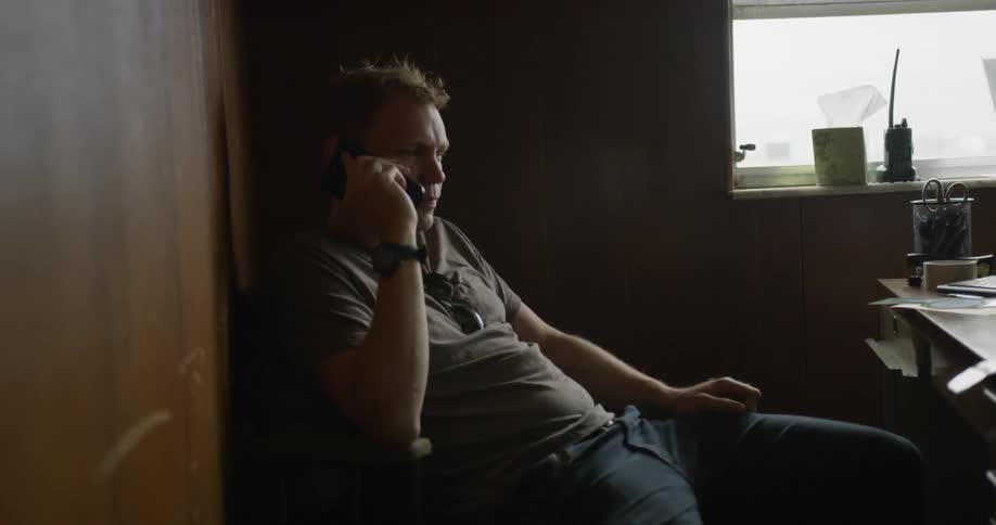 A man talks on a phone while sitting at a desk