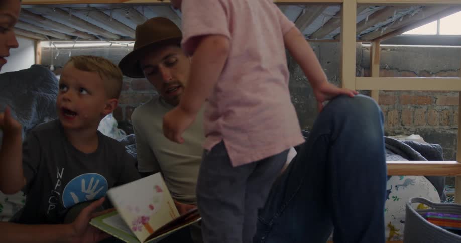 Two boys sit on a bunk bed with a man and woman reading a book
