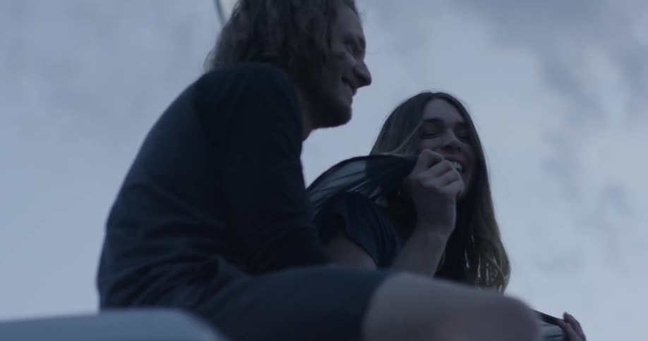 A man and woman smile and laugh outside at sunset