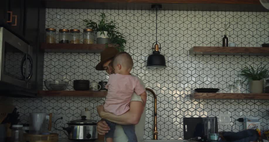 Man carries a child while standing in the kitchen