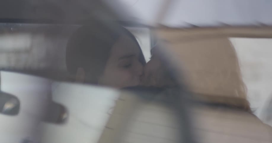 A man and woman kiss in a parked car