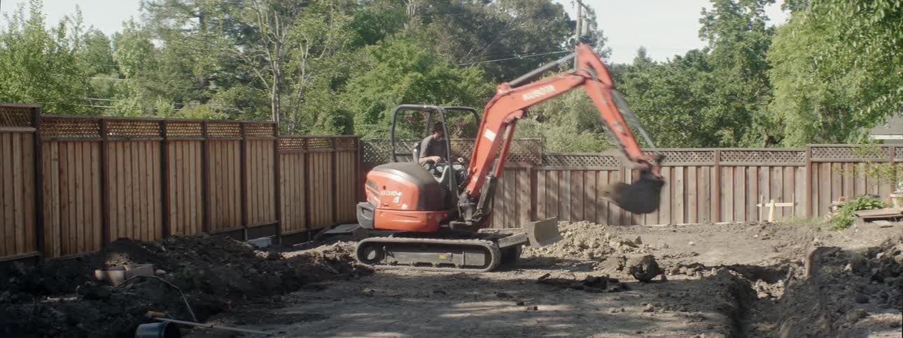 A backhoe digs in a yard