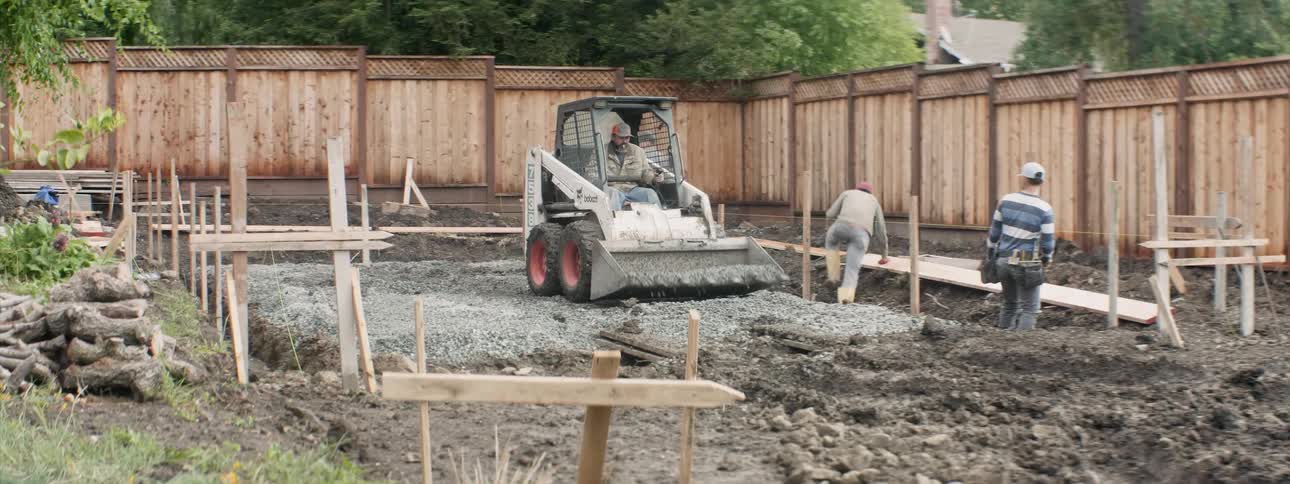 A bulldozer moves gravel in a backyard