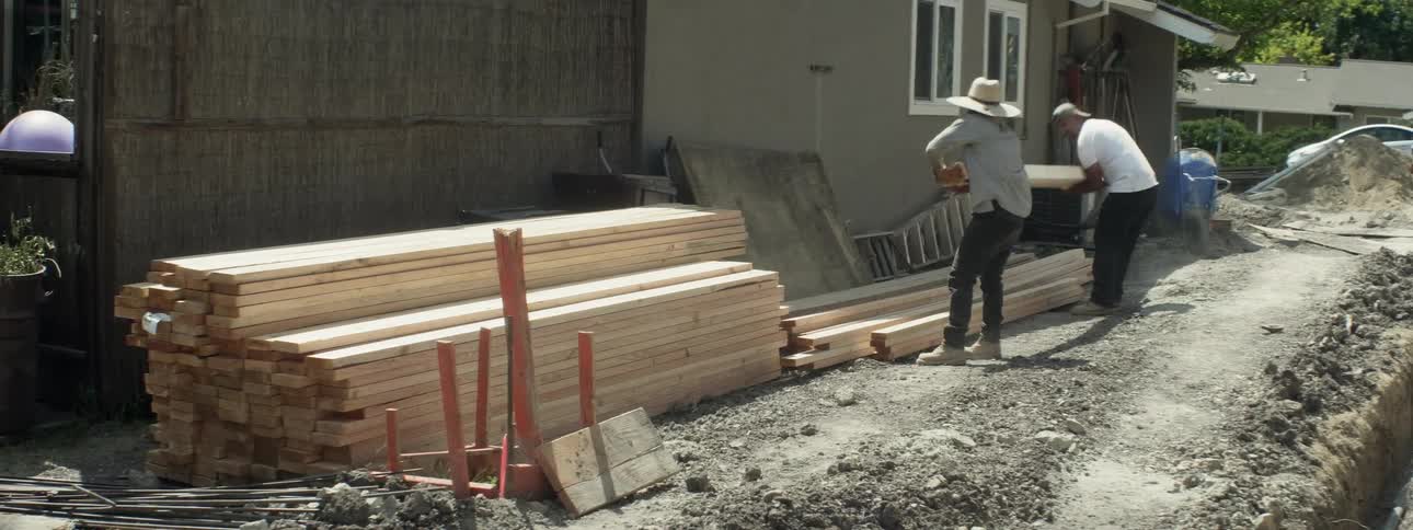 Two men set wooden beams onto a stack