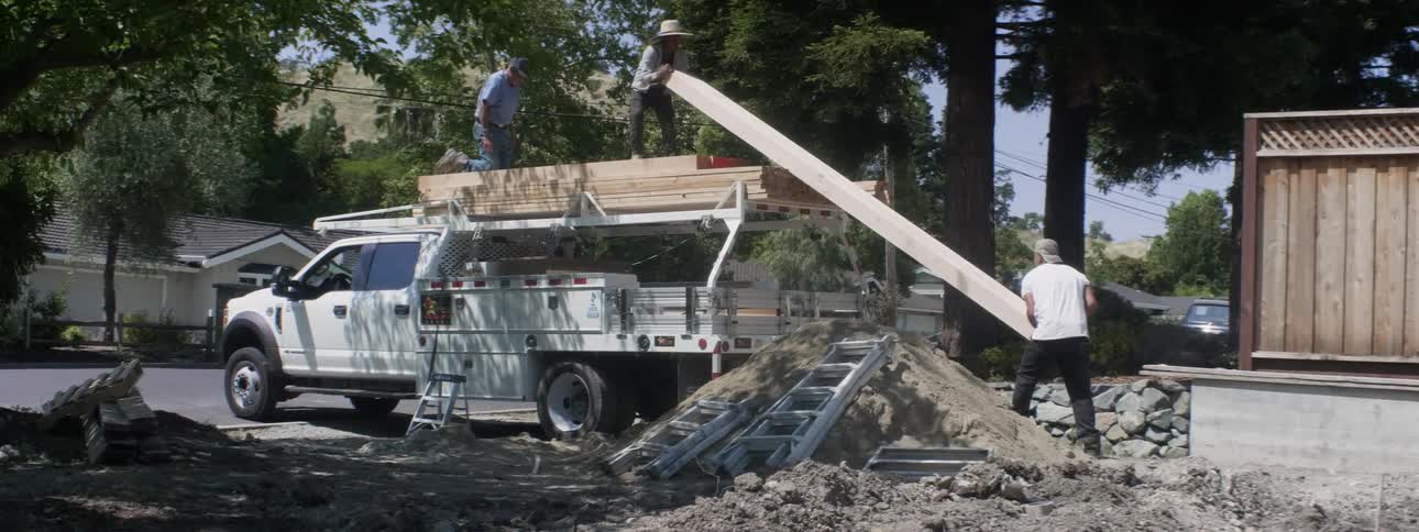 A group of men unload large wood beams off a truck at a construction site