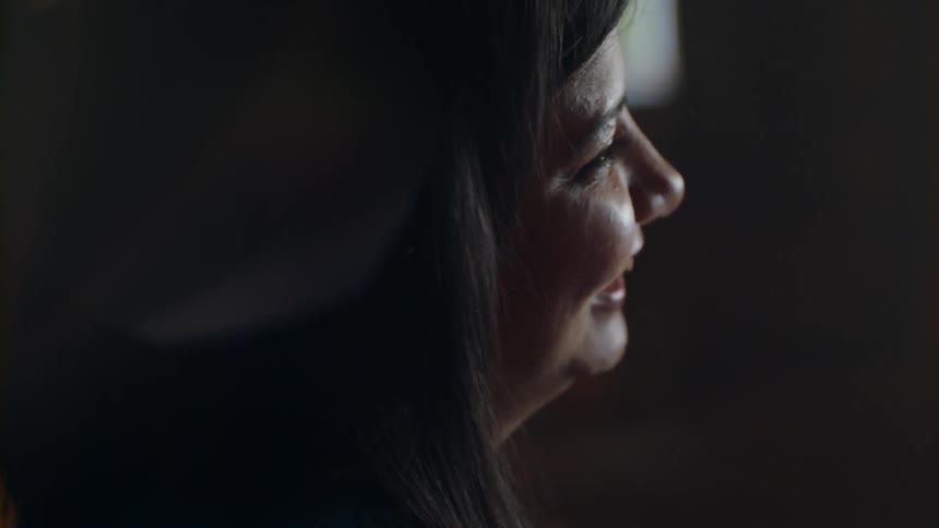 A woman laughs and talks as she sits in a dark room