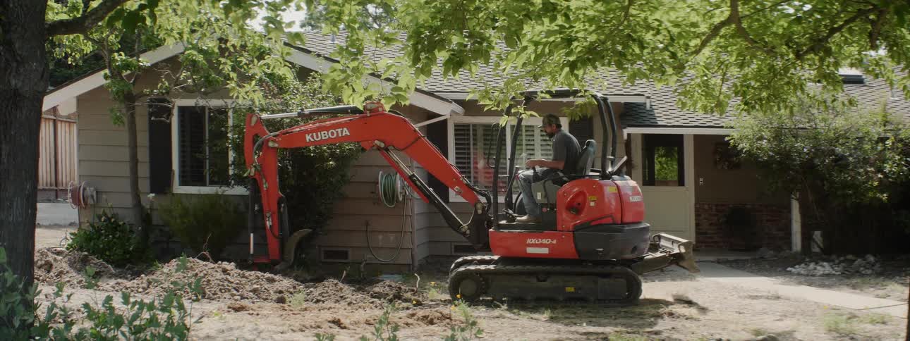 An excavator digs up dirt next to a house