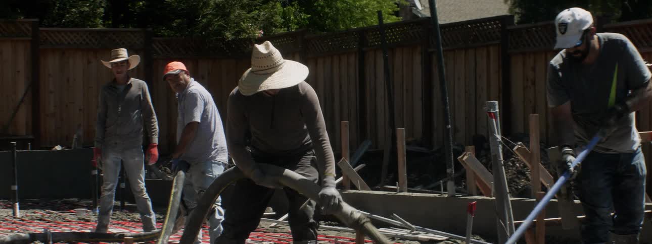 Men lay concrete through a hose at a construction site