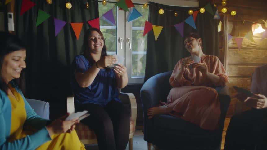 A group of women sit and laugh as they play cards at a party