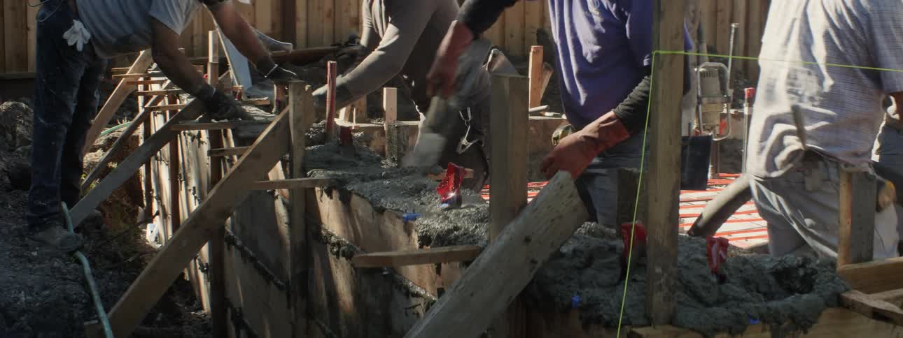 Construction workers smooth the poured cement for a wall