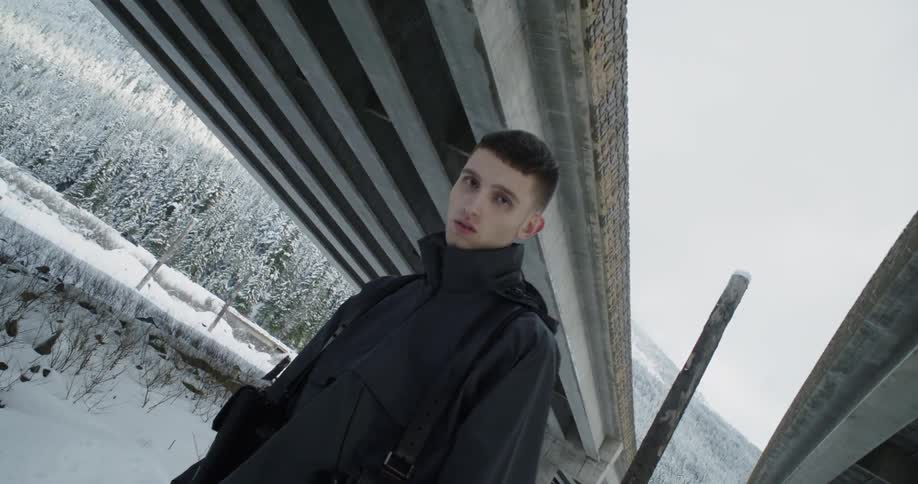 Man stands in the snow under a bridge