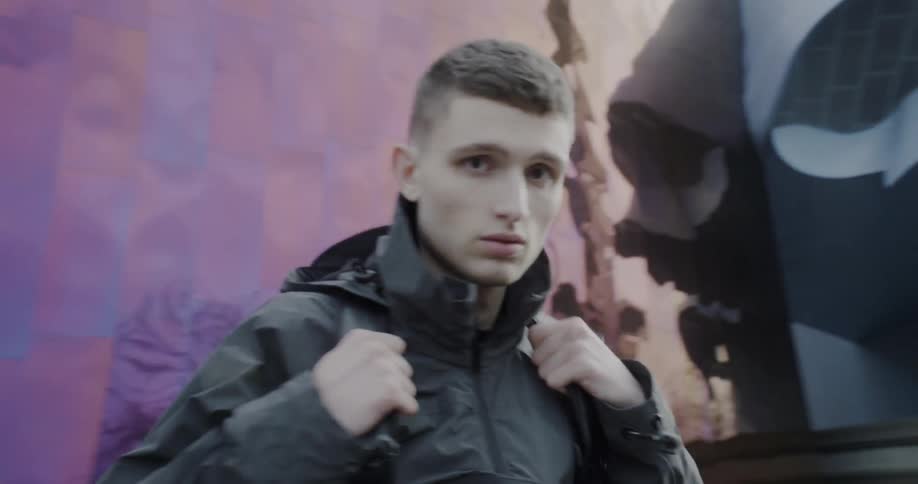 A man sits outside adjusting the straps of his backpack