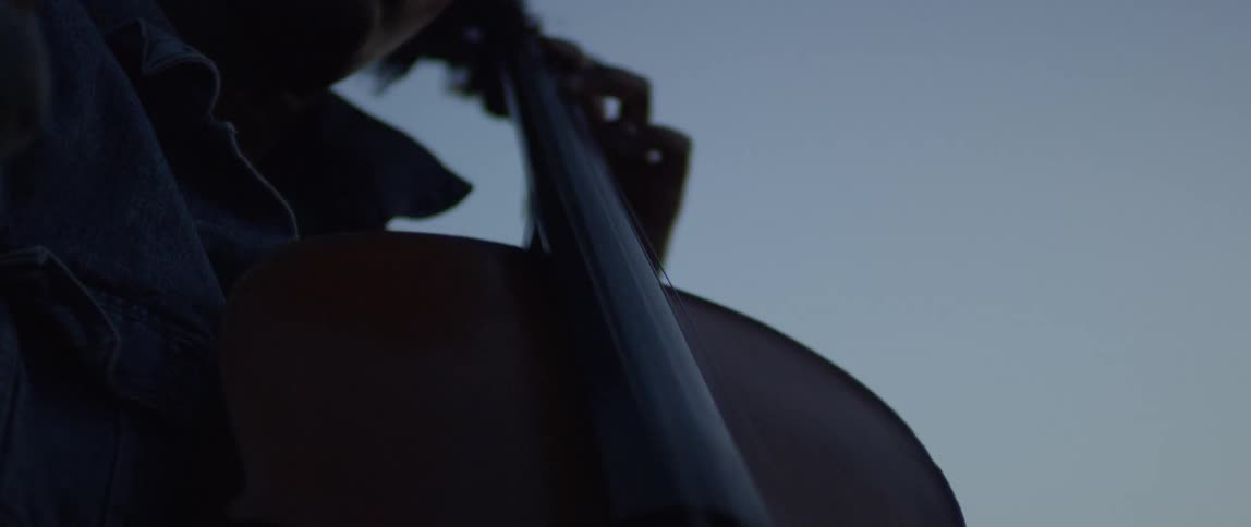 A woman plays the cello outside at dusk