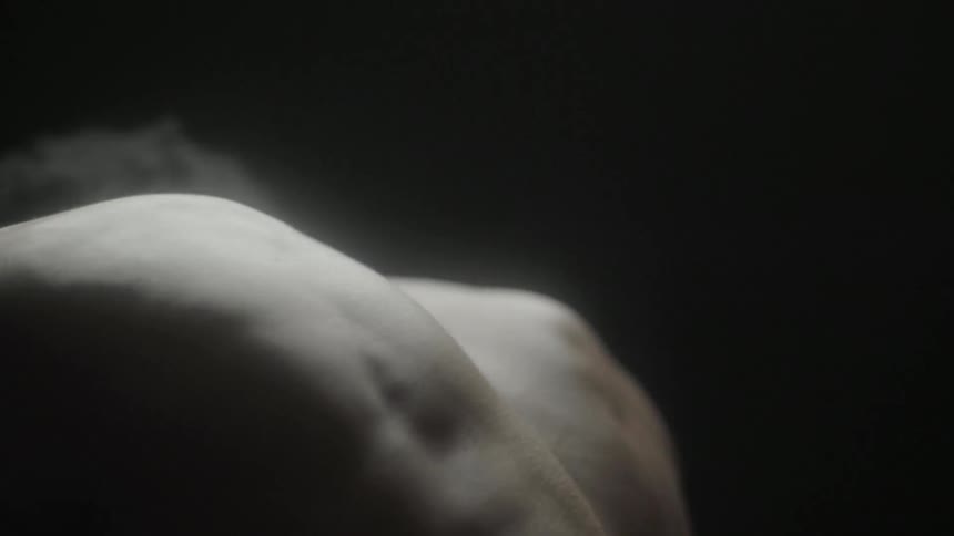 A shirtless man rubs his shoulder and arches back