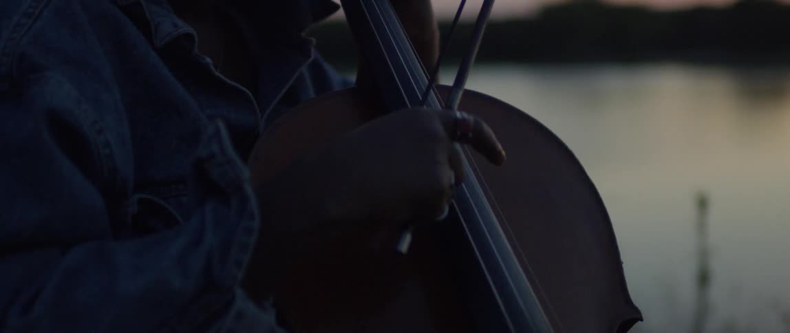 A woman stands on the beach at sunset playing the cello