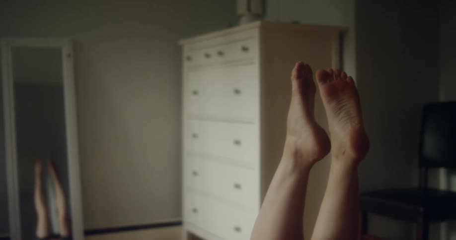 A woman lays on the floor in a dark bedroom rocking back and forth with her feet in the air