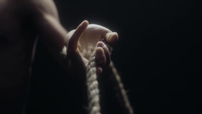 A man stands in the dark holding a rope as it moves