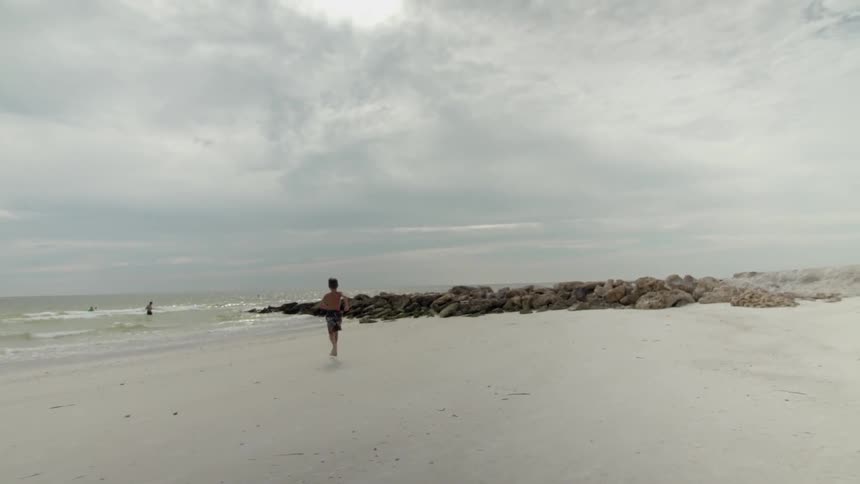 A boy running down an empty beach during the day
