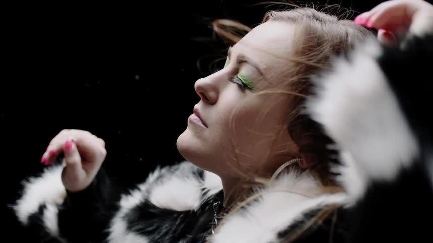 Woman wearing a fur jacket letting the wind blow through her hair in a dark room