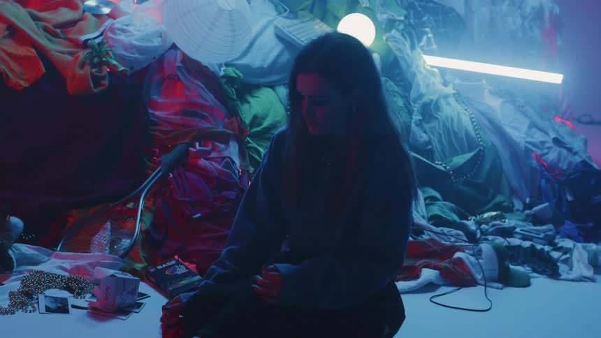 The woman is sitting near a huge pile of clothes