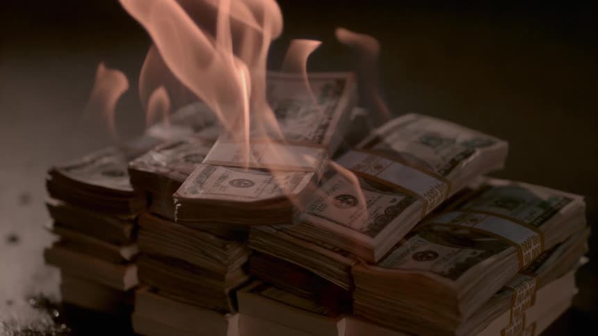 Stacks of money on fire on the floor in a dark room
