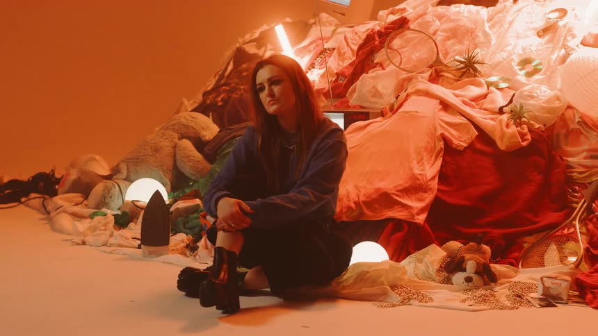 A woman sits in front of a pile of random objects