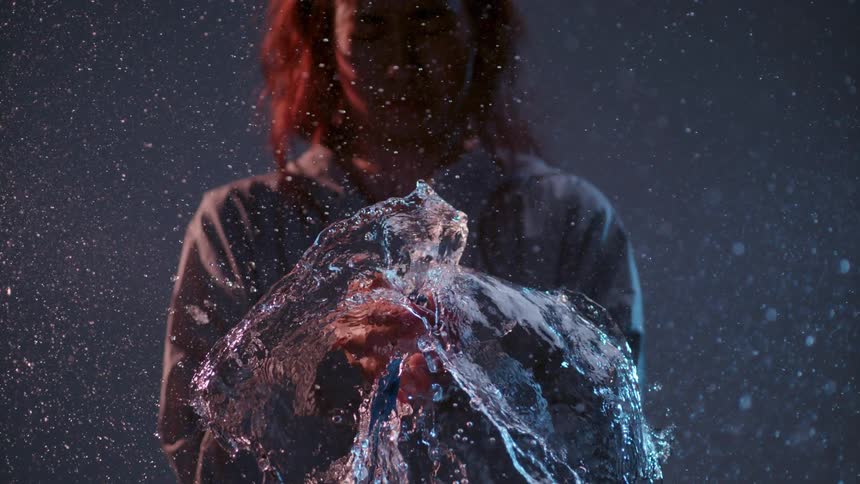 A woman holds a water balloon as it pops in slow motion