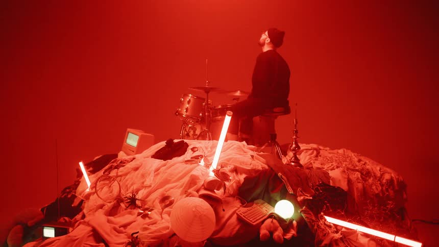 A man plays drums on a pile of random objects