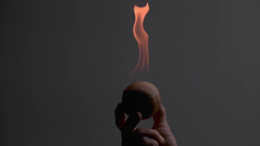 A person is holding a baseball on fire