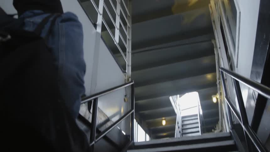 A woman carrying a bag climbs up metal steps toward sunlight