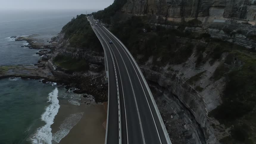 The cars travel on the road near the water