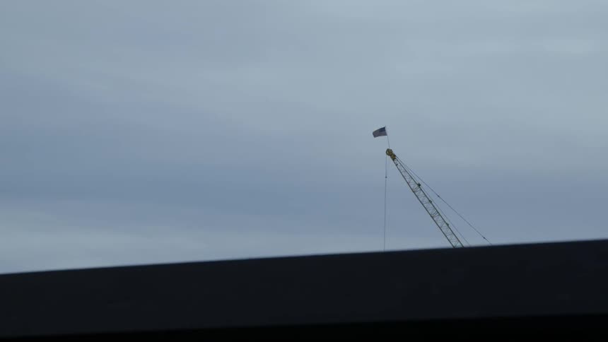 An american flag on top of a crane blows in the wind