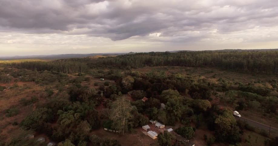 Aerial view of a road in a rural area with a homestead, trees and brownish-red dirt